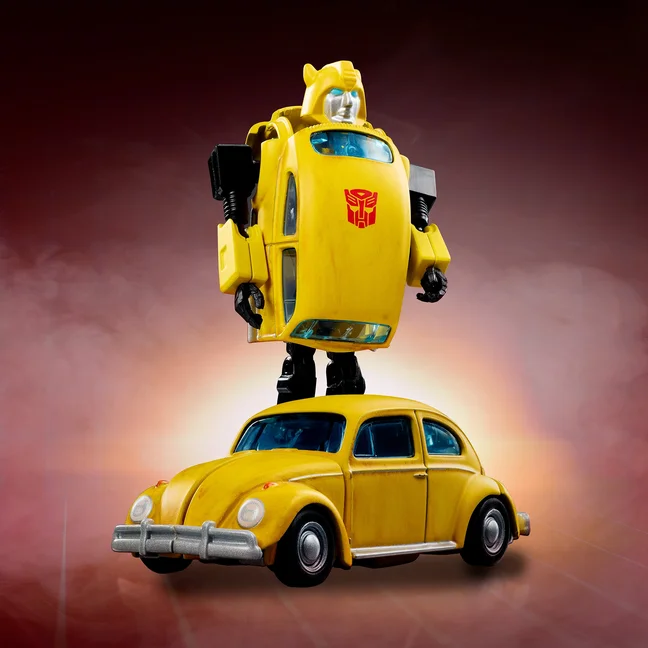 The Hot Wheels Transformers Bumblebee in robot mode standing behind the same figure shown as a yellow Volkswagen Beetle, on a red backdrop.