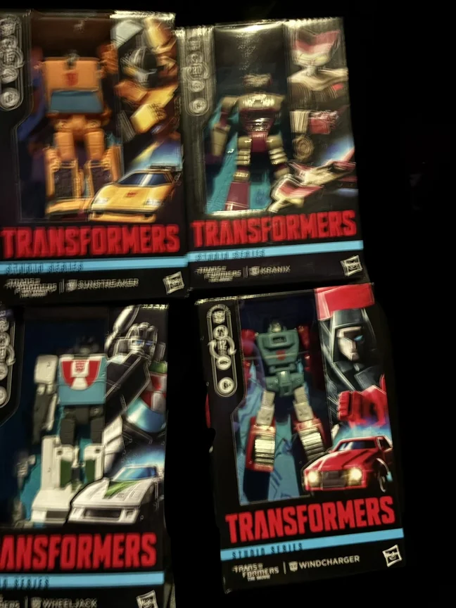 Four Transformers Studio Series Deluxe boxes laid out on a dark table, photographed at the screening. The bottom panels read TRANSFORMERS THE MOVIE SUNSTREAKER, TRANSFORMERS THE MOVIE KRANIX, TRANSFORMERS THE MOVIE WHEELJACK and TRANSFORMERS THE MOVIE WINDCHARGER