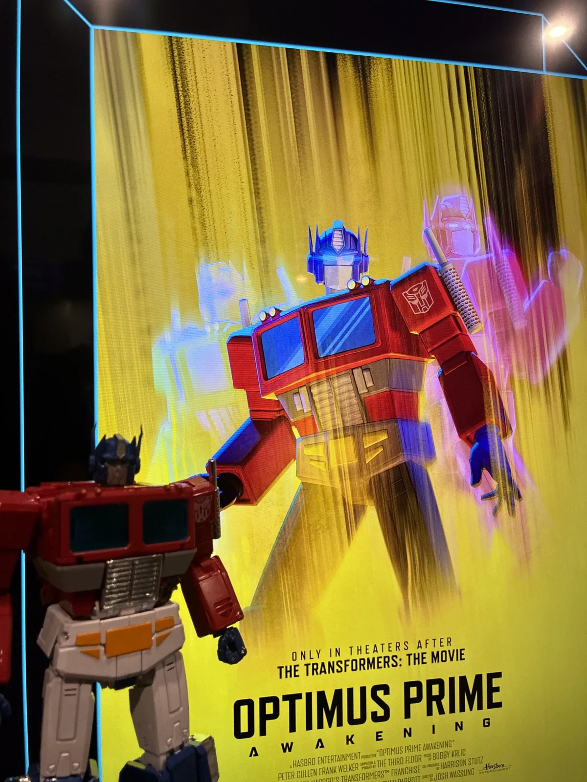 The Optimus Prime Awakening poster lit in a cinema lightbox, Optimus Prime standing against a yellow background above the billing block