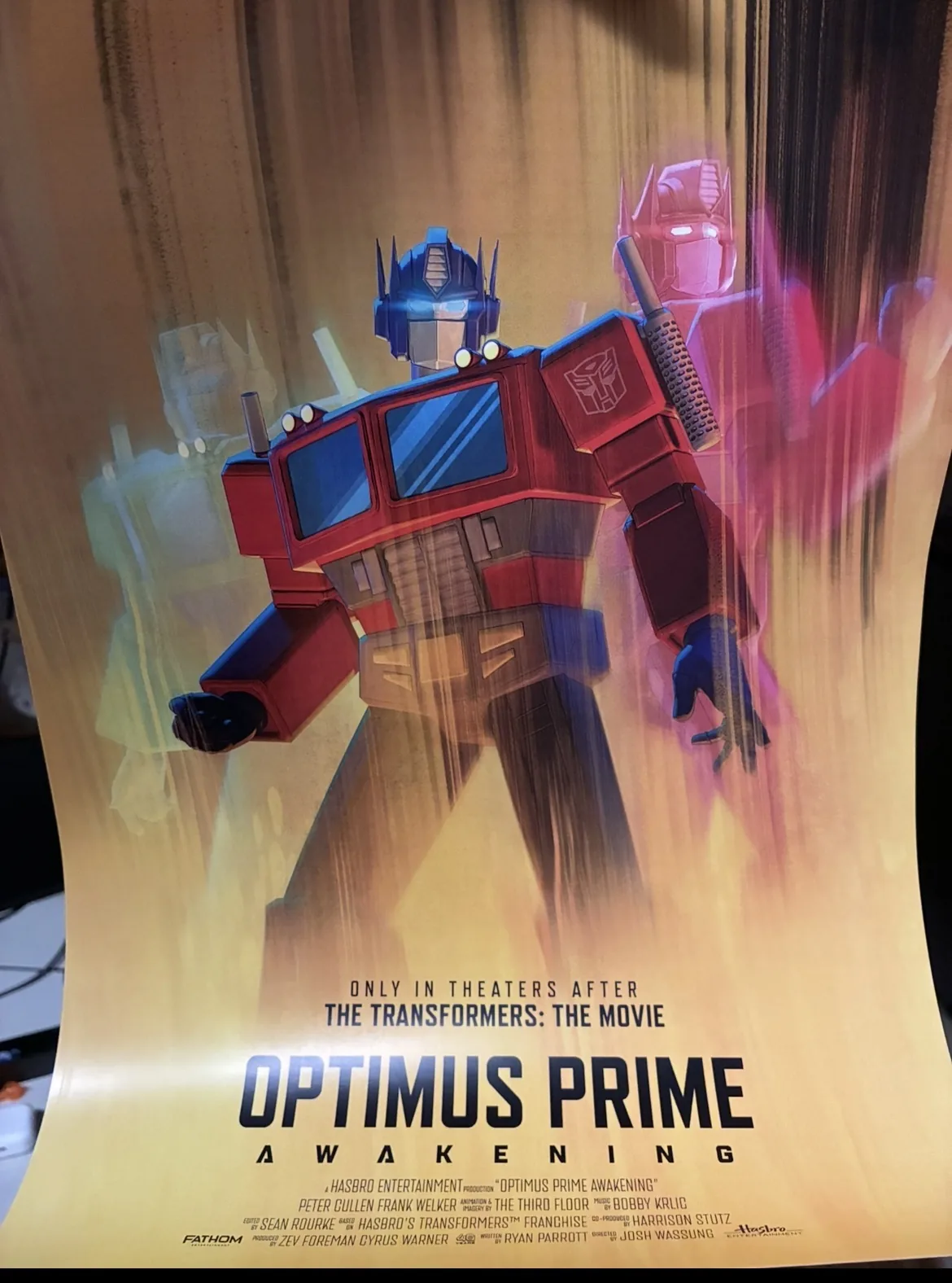 The Optimus Prime Awakening poster on a curtain, reading ONLY IN THEATERS AFTER THE TRANSFORMERS THE MOVIE above the title and the billing block