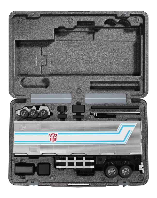 The Trailer Kit packed in an open grey hard case with cut foam. The lower half holds the assembled trailer, the Roller scout car, two grey ramp plates and several black connector parts, each in its own recess. The upper half is a moulded foam tray with empty cutouts for the remaining pieces.