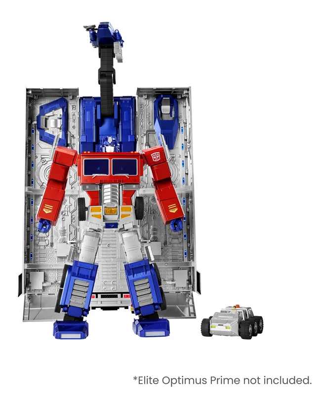 The trailer standing open on its end in Command Base mode, its two silver interior walls spread wide and crowded with moulded machinery, with a turret on a black arm rising above it. The Elite Optimus Prime figure stands in front of the opening in red and blue, and the silver Roller scout car sits at his feet. Robosen's caption reads, Elite Optimus Prime not included.